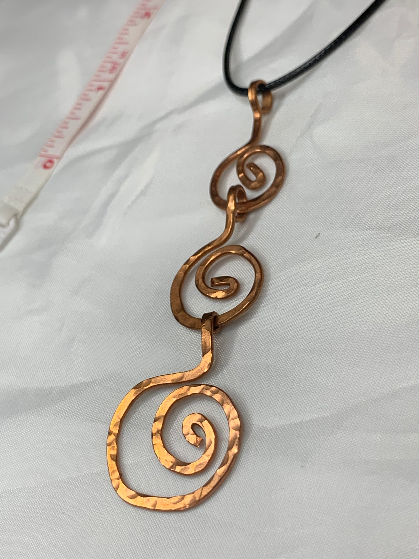 The pendant features a stunning hammered copper design, meticulously handcrafted to form an intricate spiral, symbolizing growth, evolution, and the interconnectedness of mind, body, and spirit—representing the trinity in its purest form.