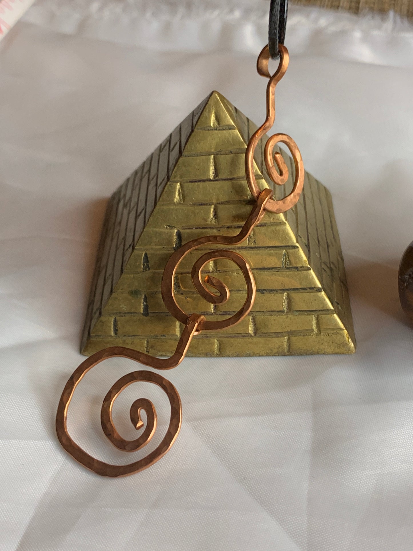 The pendant features a stunning hammered copper design, meticulously handcrafted to form an intricate spiral, symbolizing growth, evolution, and the interconnectedness of mind, body, and spirit—representing the trinity in its purest form.